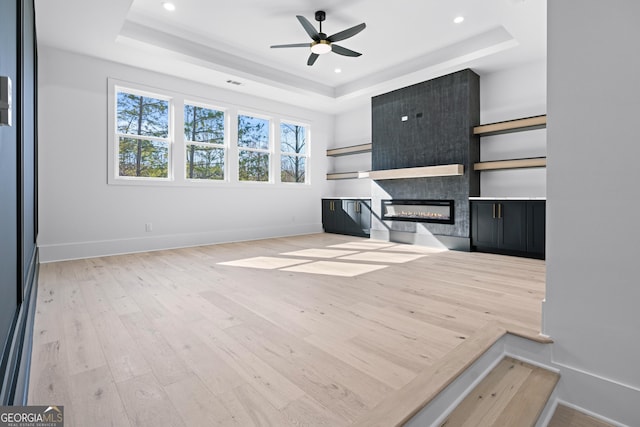 unfurnished living room featuring light hardwood / wood-style flooring, a fireplace, a raised ceiling, and ceiling fan