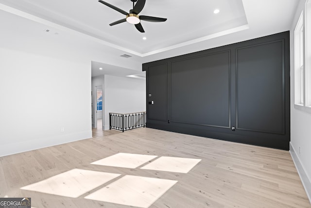 empty room featuring a tray ceiling, ceiling fan, and light hardwood / wood-style flooring