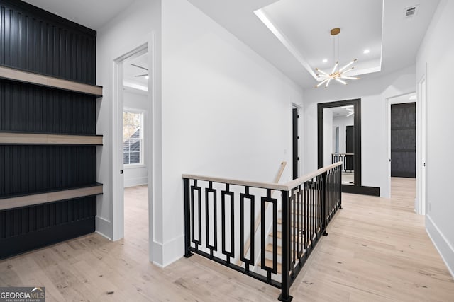 hall with a chandelier, a raised ceiling, and light hardwood / wood-style floors