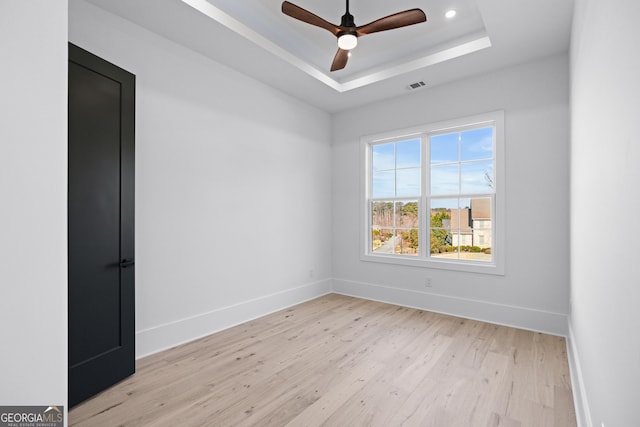 empty room with a tray ceiling, light hardwood / wood-style floors, and ceiling fan