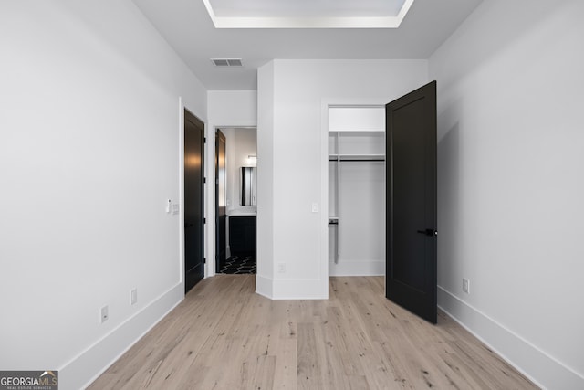 unfurnished bedroom with ensuite bath, light wood-type flooring, and a closet