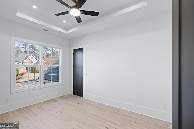 empty room featuring a tray ceiling, light hardwood / wood-style flooring, and ceiling fan