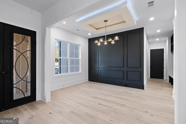 entrance foyer featuring an inviting chandelier, a tray ceiling, and light hardwood / wood-style flooring