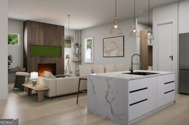 kitchen featuring sink, white cabinetry, decorative light fixtures, a center island with sink, and stainless steel refrigerator