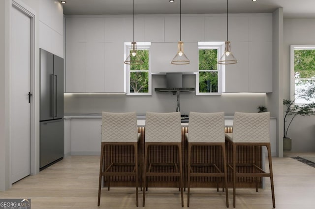 kitchen with decorative light fixtures, light wood-type flooring, stainless steel refrigerator, plenty of natural light, and white cabinets