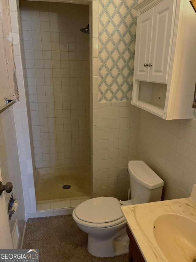 bathroom featuring a tile shower, vanity, tile walls, and toilet