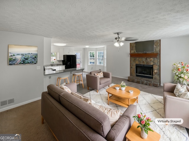 living room with ceiling fan, a fireplace, light carpet, and a textured ceiling