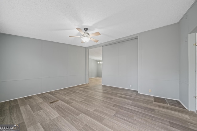 unfurnished room with ceiling fan with notable chandelier, a textured ceiling, and light wood-type flooring