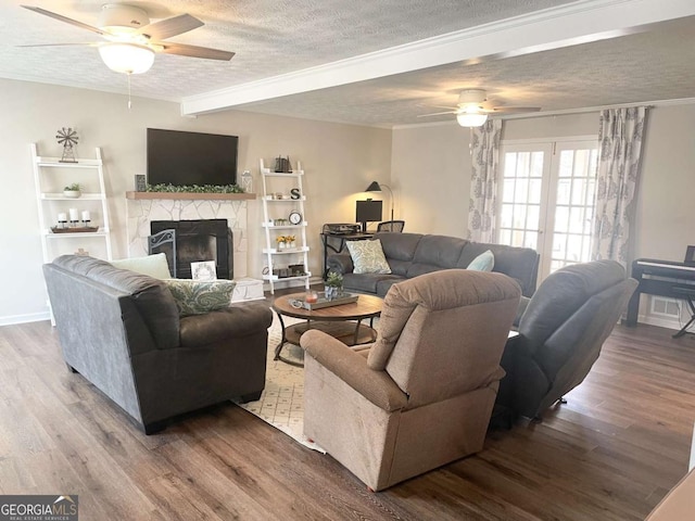 living room with ceiling fan, beam ceiling, wood-type flooring, a textured ceiling, and a stone fireplace