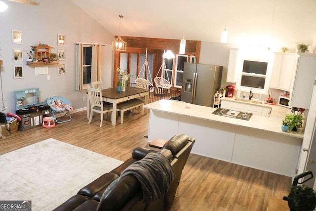 kitchen with decorative light fixtures, high vaulted ceiling, stainless steel fridge with ice dispenser, kitchen peninsula, and white cabinets