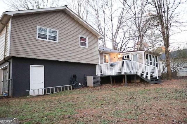 rear view of property featuring a sunroom, a lawn, a deck, and central air condition unit