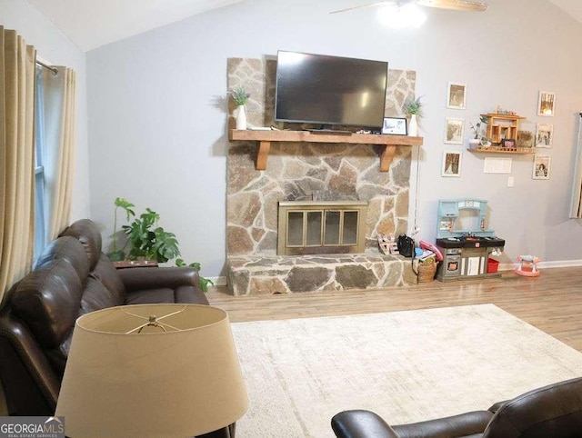 living room with vaulted ceiling, a stone fireplace, hardwood / wood-style floors, and ceiling fan