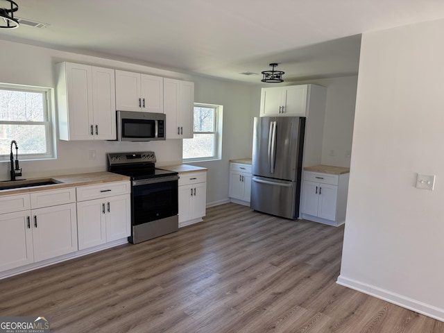 kitchen with light wood-style flooring, stainless steel appliances, a sink, white cabinets, and light countertops