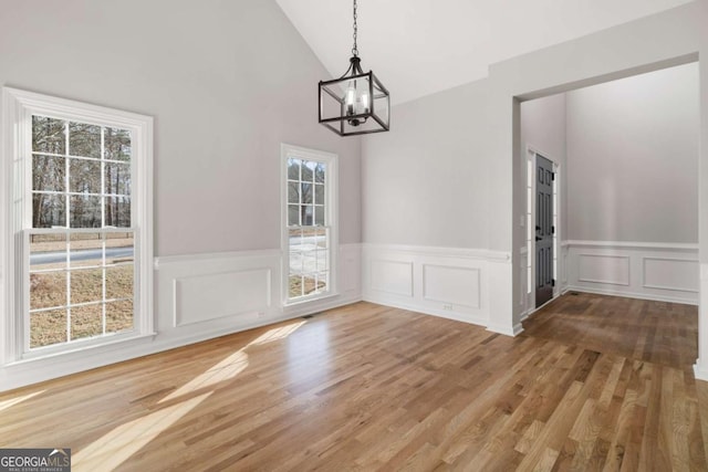 unfurnished dining area with lofted ceiling, hardwood / wood-style floors, and an inviting chandelier