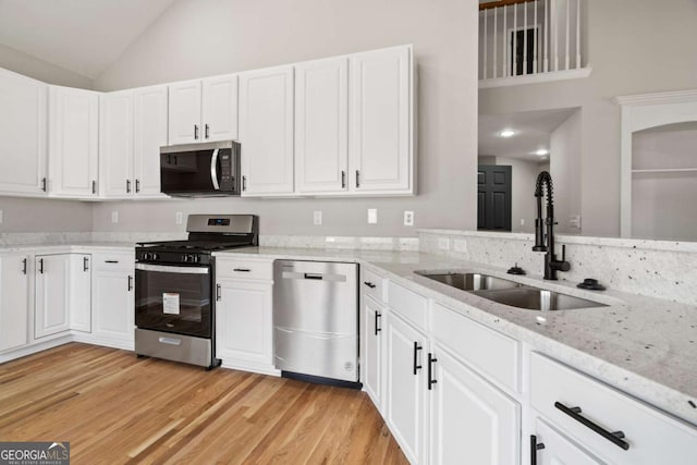 kitchen with stainless steel appliances, white cabinetry, light stone countertops, and sink