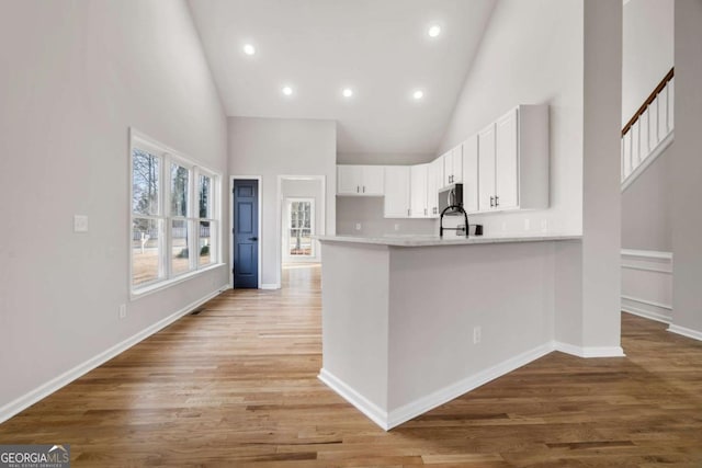 kitchen with sink, high vaulted ceiling, kitchen peninsula, light hardwood / wood-style floors, and white cabinets