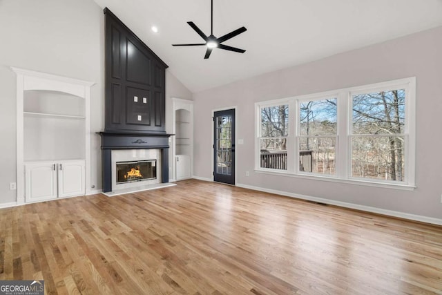 unfurnished living room with ceiling fan, a large fireplace, high vaulted ceiling, and light wood-type flooring