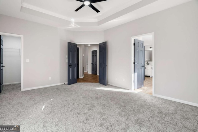 unfurnished bedroom with a walk in closet, a raised ceiling, ceiling fan, and ensuite bathroom