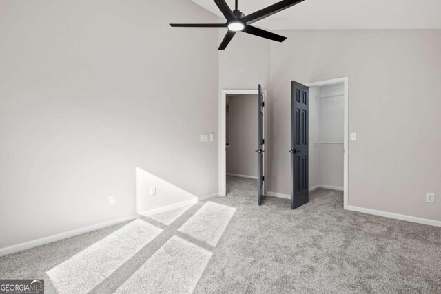 unfurnished bedroom featuring ceiling fan, high vaulted ceiling, light colored carpet, and a walk in closet