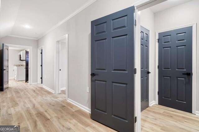 corridor with lofted ceiling, ornamental molding, and light wood-type flooring