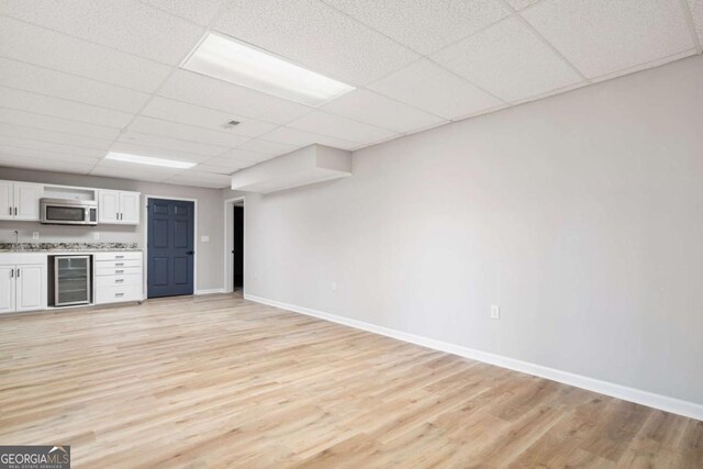 kitchen with wine cooler, a paneled ceiling, white cabinetry, and light hardwood / wood-style flooring