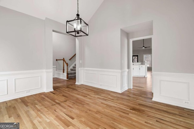 unfurnished dining area with lofted ceiling, a chandelier, and light wood-type flooring