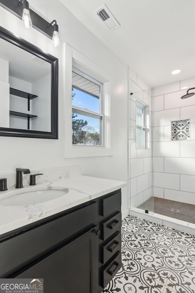 bathroom with a tile shower, vanity, and tile patterned flooring