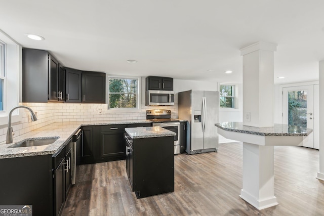 kitchen featuring sink, backsplash, a center island, light stone counters, and stainless steel appliances