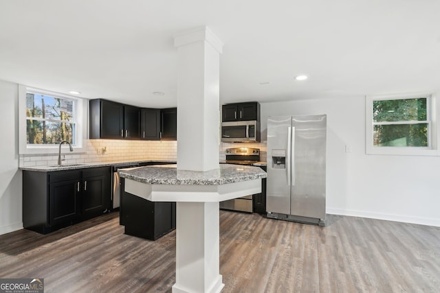 kitchen with appliances with stainless steel finishes, a center island, light stone countertops, and backsplash