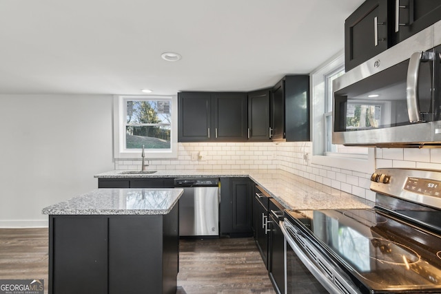 kitchen featuring backsplash, stainless steel appliances, dark hardwood / wood-style floors, light stone countertops, and a kitchen island