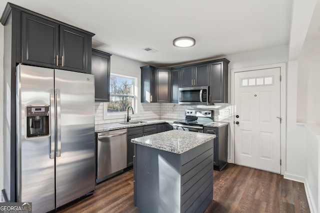 kitchen featuring a kitchen island, appliances with stainless steel finishes, tasteful backsplash, sink, and light stone counters