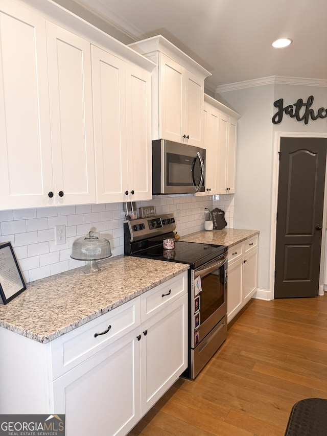 kitchen with light stone counters, light wood-type flooring, white cabinets, and appliances with stainless steel finishes