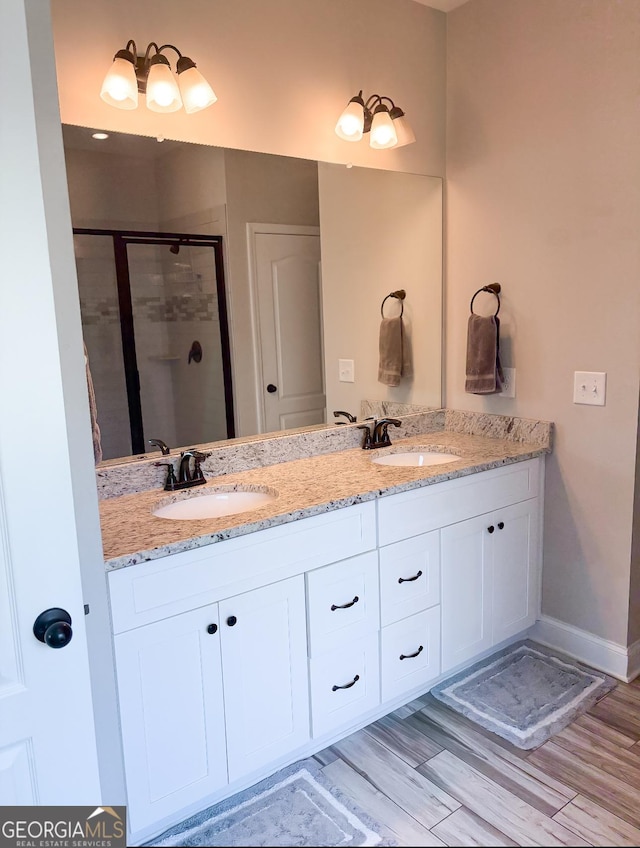 bathroom featuring a sink, a stall shower, double vanity, and wood finished floors