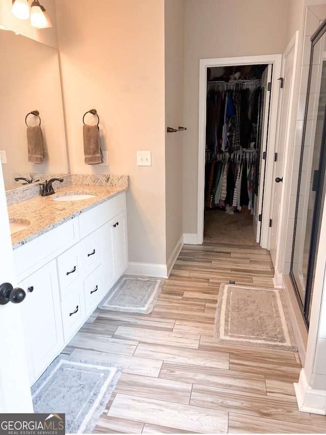 bathroom with double vanity, a walk in closet, a stall shower, wood finished floors, and a sink