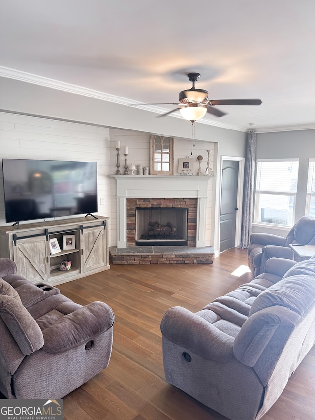 living area with ceiling fan, ornamental molding, wood finished floors, and a stone fireplace