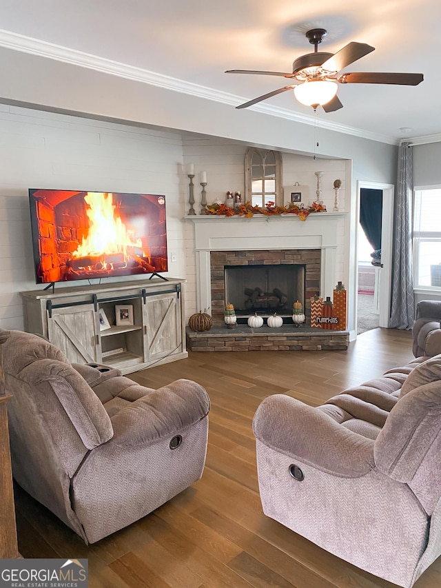 living room featuring hardwood / wood-style flooring, ceiling fan, ornamental molding, and a fireplace