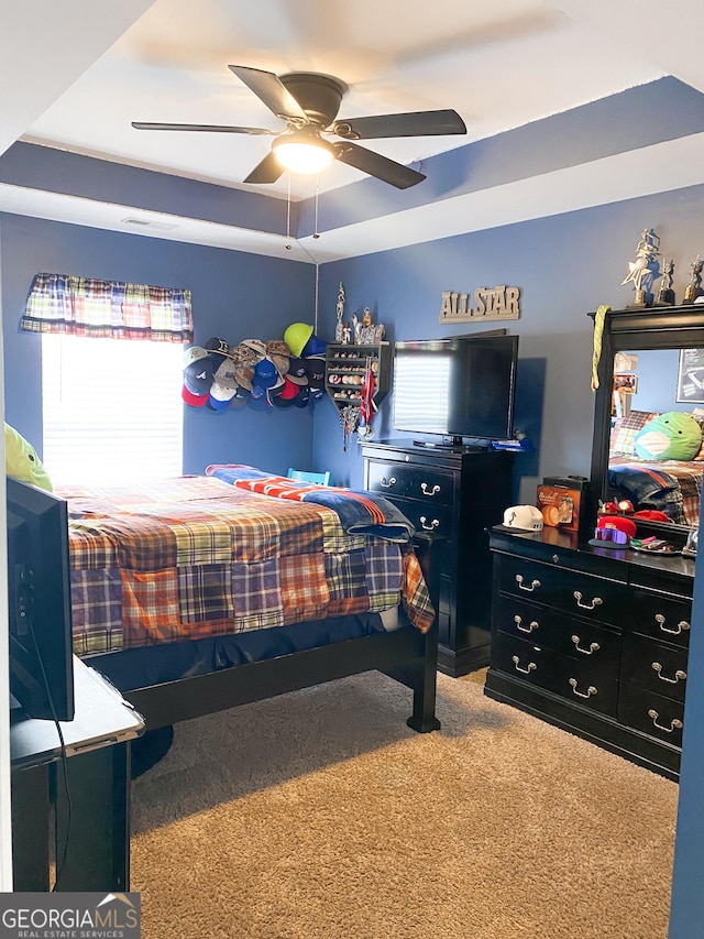 carpeted bedroom featuring a raised ceiling, ceiling fan, and multiple windows