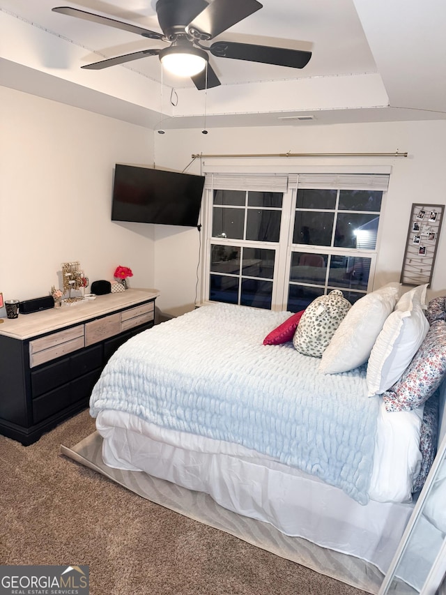 carpeted bedroom featuring ceiling fan and a raised ceiling