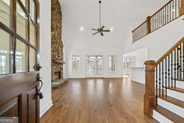 living room featuring hardwood / wood-style floors, a towering ceiling, a stone fireplace, and ceiling fan with notable chandelier