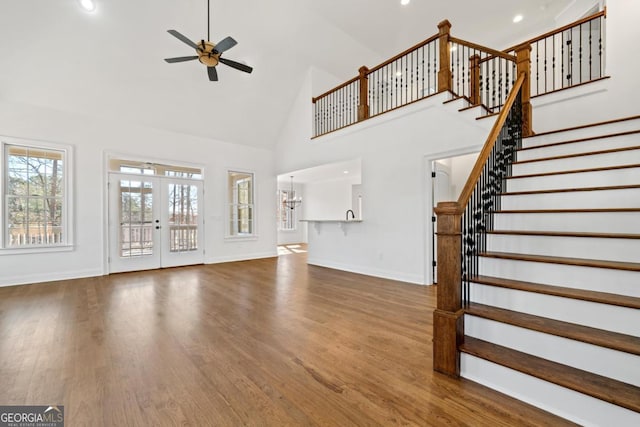 unfurnished living room featuring ceiling fan, hardwood / wood-style floors, high vaulted ceiling, and french doors