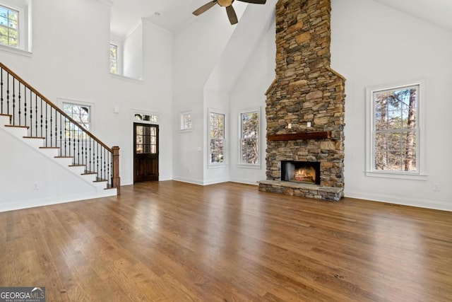 unfurnished living room with a towering ceiling, a healthy amount of sunlight, a stone fireplace, and hardwood / wood-style floors