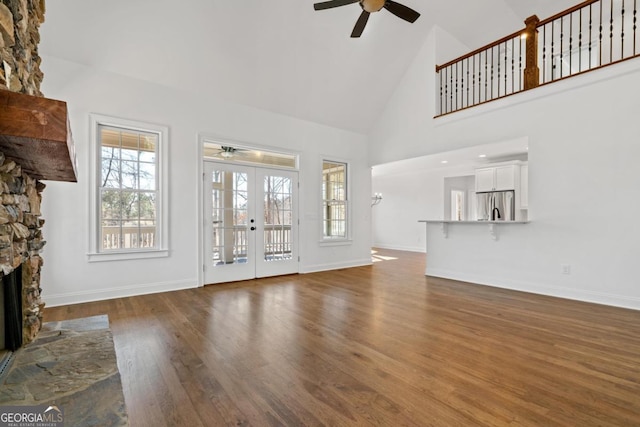 unfurnished living room with a stone fireplace, high vaulted ceiling, ceiling fan, dark wood-type flooring, and french doors