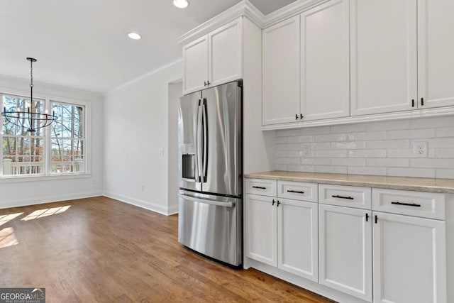 kitchen with crown molding, stainless steel fridge, light stone countertops, decorative backsplash, and white cabinets