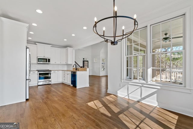 kitchen with sink, white cabinets, stainless steel appliances, ceiling fan with notable chandelier, and backsplash