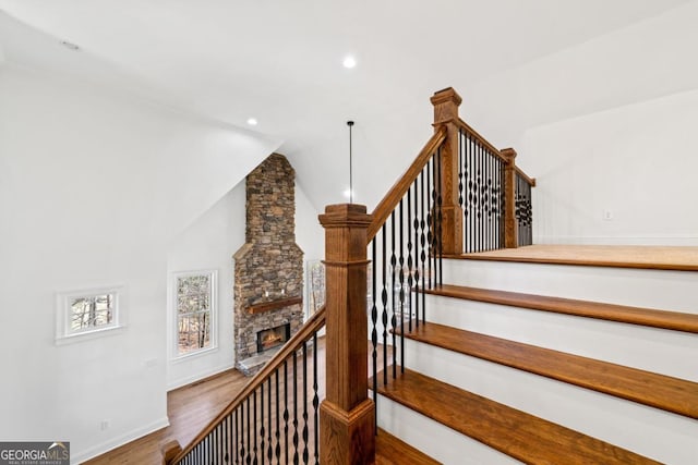 staircase with vaulted ceiling, a stone fireplace, and wood-type flooring