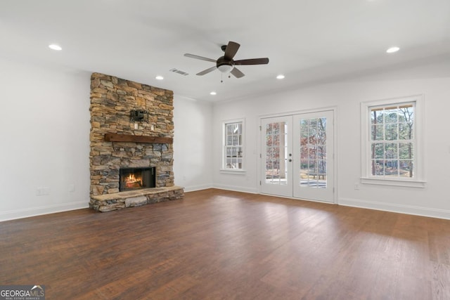 unfurnished living room featuring a stone fireplace, dark wood-type flooring, french doors, and ceiling fan