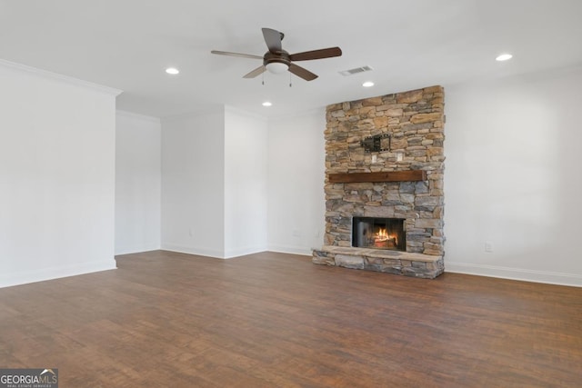 unfurnished living room with dark wood-type flooring, ceiling fan, ornamental molding, and a stone fireplace