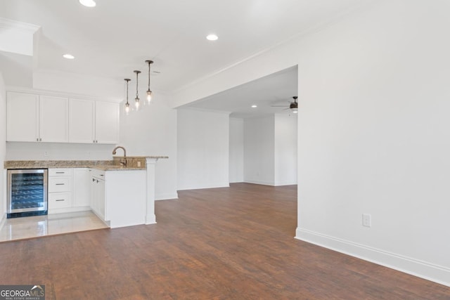 kitchen featuring wine cooler, light stone counters, hanging light fixtures, kitchen peninsula, and white cabinets