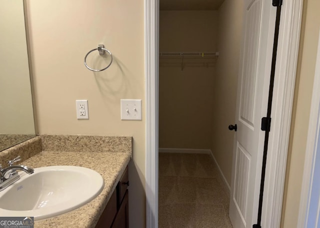 bathroom with baseboards, a walk in closet, and vanity