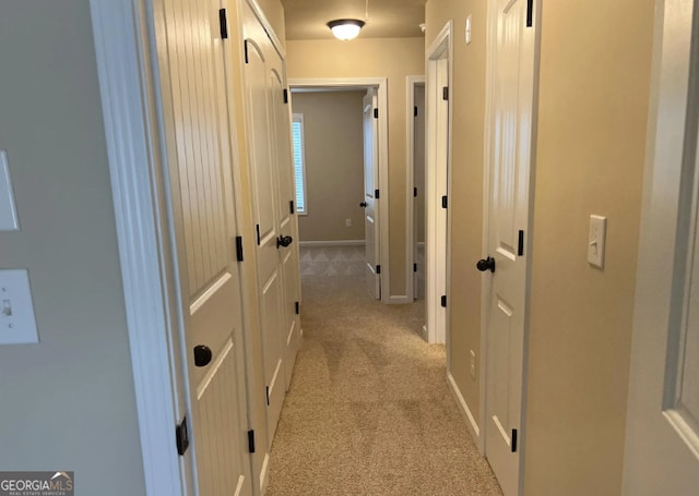 corridor with baseboards and light colored carpet